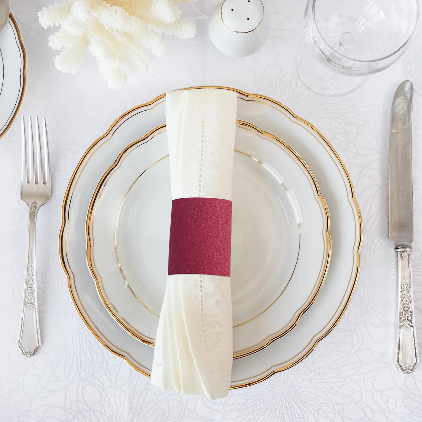 White napkin secured with a burgundy paper band on a gold-rimmed plate
